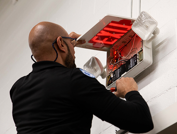 Tech Repairing an Exit and Emergency Light